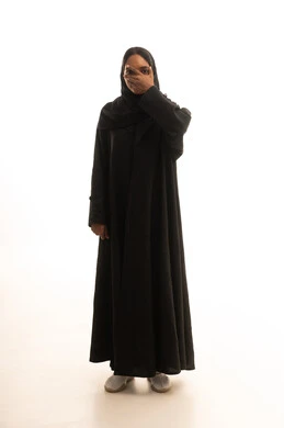 Eye health and regular vision examinations, a portrait of a Saudi Gulf Arab woman wearing an abaya and hijab pointing to a sign indicating a vision test, full-body, white background.