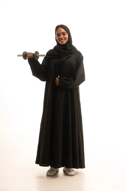 Maintaining health and physical fitness, practicing sports and lifting weights with dumbbells, a portrait of a Gulf Arab Saudi university student wearing an abaya and hijab holding heavy weights in her hand, white background.