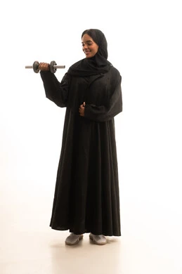 Practicing sports and lifting weights with dumbbells, a portrait of a Gulf Arab Saudi university student wearing an abaya and hijab, holding heavy weights in her hand, maintaining health and physical fitness, white background.