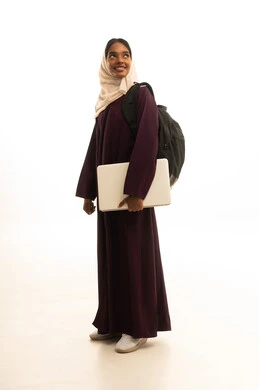 Using a laptop, research and scientific studies, a portrait of a Saudi Arabian Gulf Arab university student with dark skin wearing an abaya and hijab and carrying a backpack using a laptop, advanced academic universities in Saudi Arabia.