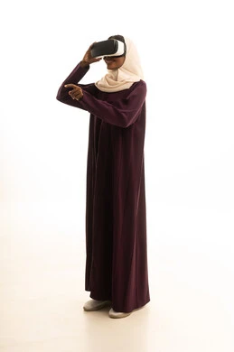 Using virtual reality glasses, expressions of immersion and focus, setting a specific goal, a portrait of a Gulf Arab Saudi woman wearing an abaya and hijab, wearing VR glasses, with a white background.