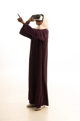 تعابير الاندماج والتركيز، استخدام نظارات الواقع الافتراضي ،تحديد هدف ما ، بورتريه لامراه عربية خليجية سعودية ترتدي العباءه والحجاب ترتدي نظارات الفي ار، خلفيه بيضاء