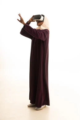 استخدام نظارات الواقع الافتراضي ، تعابير الاندماج والتركيز،تحديد هدف ما ، بورتريه لامراه عربية خليجية سعودية ترتدي العباءه والحجاب ترتدي نظارات الفي ار، خلفيه بيضاء