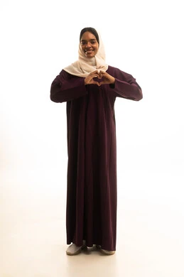 ايماءات يدين على شكل قلب، اظهار مشاعر الحب والشغف، مفهوم المحبة والمودة، بورتريه لامرأه عربيه خليجيه سعودية ترتدي العباءة والحجاب تنظر إلى الكاميرا بتعابير السرور والسعادة، صورة لكامل الجسم، خلفية بيضاء