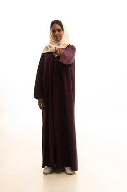 إشارات وحركات يدين تدل على هذا المكان (هنا)، بورتريه لامرأة عربية خليجية سعودية مبتسمة ترتدي الحجاب والعباءة ترفع إصبعها السبابة تشير إلى شيء ما، تحديد موقع معين ، الجسم بالطول الكامل، خلفية بيضاء