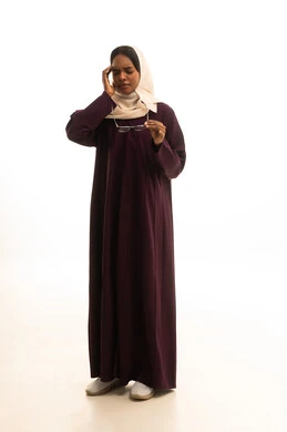 المعاناة من آلام الشقيقة، الصداع وألم الرأس،الحاجة للهدوء والراحة، إمرأة عربية خليجية سعودية ترتدي العباءة والحجاب تضع يديها على رأسها بايماءات التعب والارهاق تمسك بيدها نظارات طبية ، خلفية بيضاء