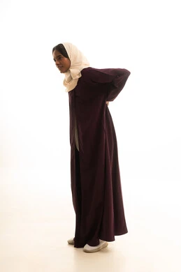 تعابير الألم ووجع الظهر، الشعور بالمرض والإرهاق، بورتريه لامرأة عربية خليجية سعودية ترتدي العباءة والحجاب تضع يدها على ظهرها بايماءات التعب، الحاجة للعلاج والاستشارة الطبية، صورة لكامل الجسم، خلفية بيضاء