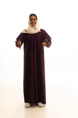 تحديد موقع معين ، بورتريه لامرأة عربية خليجية سعودية مبتسمة ترتدي الحجاب والعباءة تشير بإصبعها السبابة إلى شيء ما، إشارات وحركات يدين تدل على هذا المكان (هنا)، الجسم بالطول الكامل، خلفية بيضاء