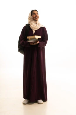 النظر بايماءات السعادة بجانباً الي شئ ما، التعليم العالي في جامعات المملكة، المناهج والمواد التعليمية الحديثة، الاستعداد للعام الجامعي الجديد، بورتريه لطالبة جامعية عربية خليجية سعودية سمراء ترتدي العباءه والحجاب وحقيبة الظهر تحمل مجموعة من الكتب ، خلفية بيضاء