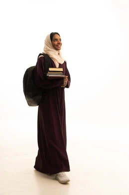 الاستعداد للعام الجامعي الجديد، المناهج والمواد التعليمية الحديثة، التعليم العالي في جامعات المملكة،بورتريه من الجانب لطالبة جامعية عربية خليجية سعودية سمراء ترتدي العباءه والحجاب وحقيبة الظهر تحمل مجموعة من الكتب ، خلفية بيضاء