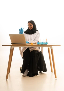 Effective learning methods by utilizing technology and technological devices, using experimental educational tools and means, a portrait of a Gulf Arab Saudi female student wearing an abaya, hijab, white coat, and protective glasses sitting in front of a testing table with sample tubes and chemical analyses, white background.