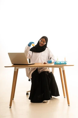 اكتساب المعرفة والخبرة، الاستفادة من التقنيات والأجهزة التكنولوجية، استخدام الأدوات والوسائل التعليمية التجريبية، بورتريه لطالبة عربيه خليجيه سعوديه ترتدي العباءه والحجاب والمعطف الابيض ونظارات الحماية تستخدم جهاز الحاسوب المحمول تجلس امام طاولة الاختبارات وأنابيب العينات والتحاليل الكيميائية، خلفية بيضاء