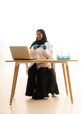 أساليب التعلم الفعال بالاستفادة من التقنيات والأجهزة التكنولوجية، استخدام الأدوات والوسائل التعليمية التجريبية، بورتريه لطالبة عربيه خليجيه سعوديه ترتدي العباءه والحجاب والمعطف الابيض ونظارات الحماية تستخدم جهاز الحاسوب المحمول تجلس امام طاولة الاختبارات وأنابيب العينات والتحاليل الكيميائية، خلفية بيضاء