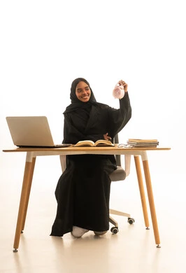 بورتريه لطالبة جامعية عربية خليجية سعودية ترتدي العباءة والحجاب امام ساعة منبه وكتب وجهاز الحاسوب المحمول , استخدام التكنولوجيا والتقنيات الحديثة ، قدوم وقت الامتحانات والمذاكرات، تطوير المناهج والمواد التعليمية في السعودية، استغلال الوقت في الدراسة والمذاكرة, خلفية بيضاء.