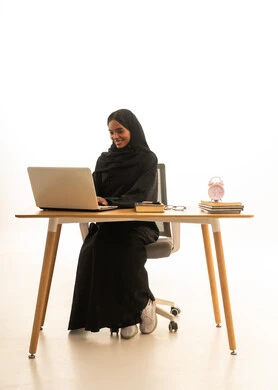 Developing curricula and educational materials in Saudi Arabia, using technology and modern techniques, the arrival of exam time and study sessions, utilizing time for studying and reviewing, a portrait of a Gulf Arab Saudi university student wearing an abaya and hijab in front of an alarm clock, books, and a laptop, with a white background.