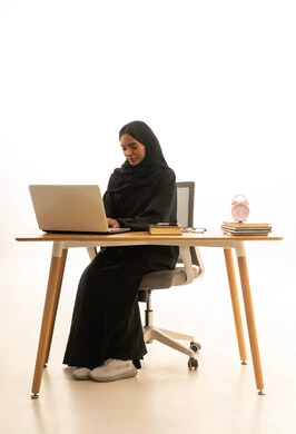 قدوم وقت الامتحانات والمذاكرات، استخدام التكنولوجيا والتقنيات الحديثة ،تطوير المناهج والمواد التعليمية في السعودية، استغلال الوقت في الدراسة والمذاكرة, بورتريه لطالبة جامعية عربية خليجية سعودية ترتدي العباءة والحجاب امام ساعة منبه وكتب وجهاز الحاسوب المحمول , خلفية بيضاء.