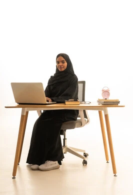 استخدام التكنولوجيا والتقنيات الحديثة ، قدوم وقت الامتحانات والمذاكرات، تطوير المناهج والمواد التعليمية في السعودية، استغلال الوقت في الدراسة والمذاكرة, بورتريه لطالبة جامعية عربية خليجية سعودية ترتدي العباءة والحجاب امام ساعة منبه وكتب وجهاز الحاسوب المحمول , خلفية بيضاء.