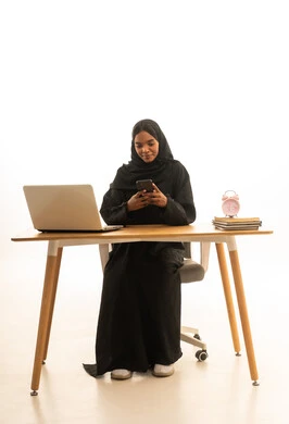 بورتريه لطالبة عربيه خليجيه سعوديه ترتدي العباءه والحجاب تستخدم جهاز اللابتوب تمسك بيدها الجوال ، تتابع حصص الاونلاين عن طريق اللابتوب،  التعلم عن بعد ، مفهوم التعليم عبر الانترنت ، استخدام التكنولوجيا والتقنيات الحديثة فى العمل ،خلفية بيضاء