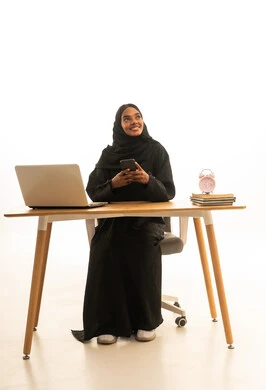 The use of mobile phones, modern technology and techniques in work, distance learning, the concept of online education, a portrait of a Gulf Arab Saudi female student wearing an abaya and hijab using a laptop, following online classes through the laptop, white background.