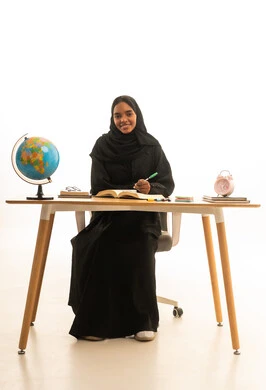 بورتريه لطالبة عربية خليجية سعودية ترتدي العباءة والحجاب تجلس على الطاولة امام  مجسم الكرة الارضية والكتب ، مراجعة الدروس اليومية بايماءات التفوق والاجتهاد , مفهوم البحث والاستكشاف حول العالم, خلفية بيضاء