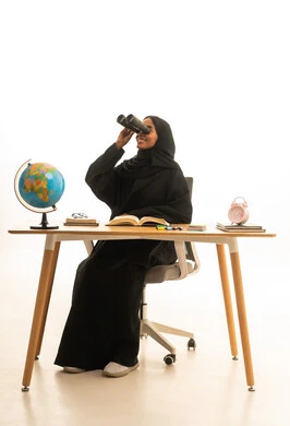Wearing virtual reality glasses, setting a specific goal, the arrival of exam time and studying, the concept of research and exploration around the world, a portrait of an Arab Gulf Saudi student wearing an abaya and hijab and VR glasses sitting at a table in front of a globe model and books, white background.