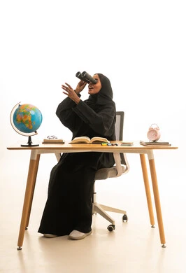 محاكاة العالم الخيالي ، تحديد هدف معين ، قدوم وقت الامتحانات والمذاكرات، مفهوم البحث والاستكشاف حول العالم, بورتريه لطالبة عربية خليجية سعودية ترتدي العباءة والحجاب ونظارات الفى ار تجلس على الطاولة امام مجسم الكرة الارضية والكتب ، خلفية بيضاء