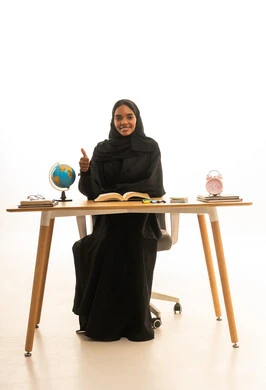 ايماءات الجودة والامتياز ، استغلال الوقت في الدراسة والمذاكرة, قدوم وقت الامتحانات والمذاكرات، مفهوم التفوق والاجتهاد , مفهوم البحث والاستكشاف حول العالم, بورتريه لطالبة عربية خليجية سعودية ترتدي العباءة والحجاب تجلس على الطاولة امام مجسم الكرة الارضية والكتب ، خلفية بيضاء