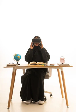 تعابير الاندماج والتركيز، تحديد هدف معين ، قدوم وقت الامتحانات والمذاكرات، مفهوم البحث والاستكشاف حول العالم, بورتريه لطالبة عربية خليجية سعودية ترتدي العباءة والحجاب ونظارات الفى ار تجلس على الطاولة امام مجسم الكرة الارضية والكتب ، خلفية بيضاء