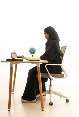 مفهوم البحث والاستكشاف حول العالم, مراجعة الدروس اليومية بايماءات التفوق والاجتهاد , بورتريه لطالبة عربية خليجية سعودية ترتدي العباءة والحجاب تجلس على الطاولة امام الحاسب المحمول و مجسم الكرة الارضية والكتب ، خلفية بيضاء