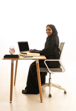 قدوم وقت الامتحانات والمذاكرات، مفهوم التفوق والاجتهاد ، استخدام التكنولوجيا والتقنيات الحديثة،بورتريه لطالبة عربية خليجية سعودية ترتدي العباءة والحجاب تجلس على الطاولة امام مجسم الكرة الارضية والكتب والحاسوب المحمول ، خلفية بيضاء