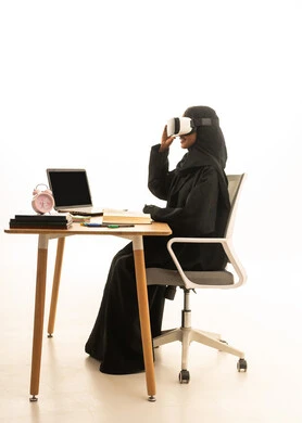 مفهوم استغلال الوقت ، استخدام التكنولوجيا والتقنيات الحديثة، قدوم وقت الامتحانات والمذاكرات، بورتريه لطالبة عربية خليجية سعودية ترتدي العباءة والحجاب ونظارات الفى ار تجلس على الطاولة امام مجسم الكرة الارضية والكتب والحاسوب المحمول ، خلفية بيضاء