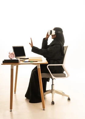 The arrival of exam and study time, the use of technology and modern techniques, setting a specific goal, the concept of research and exploration around the world, a portrait of a Gulf Arab Saudi student wearing an abaya and hijab and VR glasses sitting at a table in front of a globe model, books, and a laptop, with a white background.