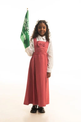 الانتماء والاعتزاز باليوم الوطني، وإحياء ذكرى اليوم الوطني السعودي في المدارس، بورتريه لطالبه عربية خليجية سعودية ترتدي الزي المدرسي والحقيبة المدرسية، تلميذه مجتهدة ترتدي الزي المدرسي الوردي تحمل بيدها علم المملكة العربية السعودية، خلفية بيضاء.