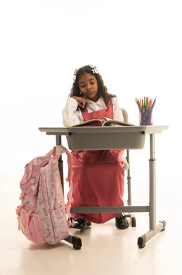 Daily lesson review, the concept of back to school, education in the Kingdom of Saudi Arabia, preparation for the new school year, a portrait of a Saudi Gulf Arab girl wearing a school uniform sitting at a desk writing in a notebook, white background.