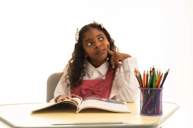 ايماءات التفكير والتمحيص، مراجعة الدروس اليومية, مفهوم العودة إلى المدارس،  التعليم في المملكة العربية السعودية, الاستعداد للعام الدراسي الجديد, بورتريه لفتاة عربية خليجية سعودية ترتدي الزي المدرسي تجلس على الطاولة المكتبية تقوم بالكتابة فى الدفتر, خلفية بيضاء