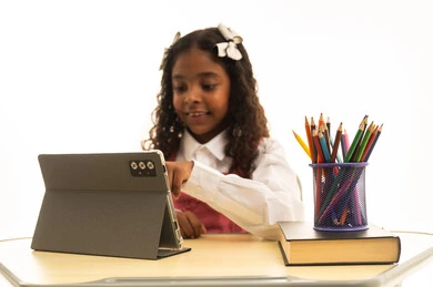 Doing homework and delivering school lectures remotely via tablet, following lessons through learning platforms, the development of science in the Kingdom of Saudi Arabia, a close-up portrait of a Gulf Arab Saudi student wearing a school uniform sitting at a desk, with a white background.