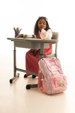 الملل والارهاق خلال الدوام، الشعور بتأخر الوقت والحاجة للنوم، موسم العودة إلى المدارس، بورتريه لطالبة عربية خليجية سعودية ترتدي الزي المدرسي  تجلس في مقعدها تقوم بالنظر إلى ساعة المنبه، قرطاسية مدرسية على الطاولة المكتبية، خلفية بيضاء