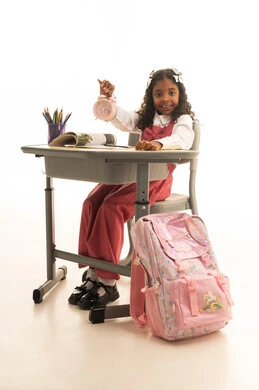 الجد والاجتهاد للوصول إلى النجاح والتفوق، موسم العودة إلى المدارس، بورتريه لطالبة عربية خليجية سعودية ترتدي الزي المدرسي  تجلس في مقعدها تقوم بالنظر إلى ساعة المنبه بسعادة، قرطاسية مدرسية على الطاولة المكتبية، خلفية بيضاء