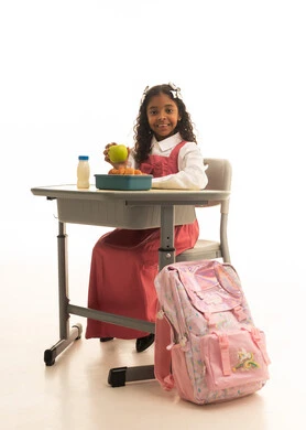 Important fruits for children's health, enjoying healthy foods during school break, back-to-school season, a portrait of a Saudi Arabian Gulf Arab student wearing a school uniform sitting at a desk, having a healthy breakfast during the school break, white background.