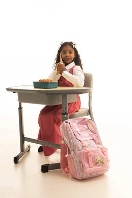 Drinking natural orange-flavored beverages, enjoying healthy foods during school break time, back-to-school season, a portrait of a Saudi Gulf Arab student wearing a school uniform sitting at a desk, having a healthy breakfast during the school break, white background.