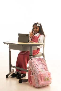 Utilizing modern technologies and technology in learning, following lessons through learning platforms, a close-up portrait of a Saudi Gulf Arab student wearing a school uniform sitting at a desk, a Saudi girl doing homework and attending school lectures remotely via a tablet, white background.