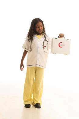 علاج أولي سريع ، التعامل مع الإصابات الشائعة و حالات الطوارئ ، بورتريه لطفلة عربية خليجية سعودية ترتدي المعطف الطبي الخاص بمهنة الطب ، تحمل بيدها حقيبة إسعافات أولية بإيماءات تدل على السعادة ، مهن مستقبلية مهمة  ، خلفية بيضاء