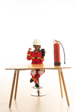 A blank black screen displayed on a mobile phone, the pursuit of dreams to achieve them, the profession of a firefighter and civil defense, a portrait of an Arab Gulf Saudi girl wearing a helmet and a special protective suit for firefighters and fire-resistant shoes sitting behind a desk using a mobile phone, white background.