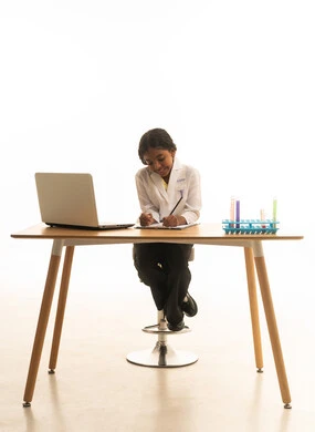 Taking notes on a computer, a passion for learning and the dream of becoming a chemical researcher, a close-up portrait of a Saudi Gulf Arab girl wearing a white lab coat, using test tubes and conducting reactions and scientific research, white background.