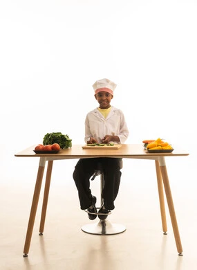 اعداد وتحضير الاطعمة و الوصفات الشهية ،سلطة صحية وخفيفة  , بورتريه لطفلة عربية خليجيه سعودية ترتدي زي الشيف مع قبعته البيضاء تقوم بتقطيع الخضراوات  بإيماءات السعادة, خلفية بيضاء