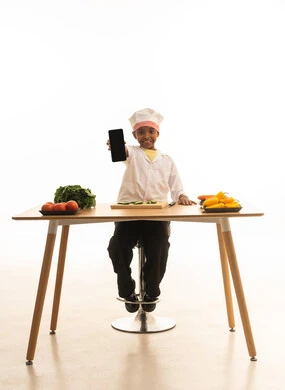 عرض تطبيقات و برامج اعداد الطبخ و الاطعمة اللذيذة ،الوصفات الشهية و المتعة في تحضيرها , بورتريه لطفلة عربية خليجيه سعودية ترتدي زي الشيف مع قبعته البيضاء, تمسك بيديها الهاتف المحمول بإيماءات الاكتشاف والسعادة, خلفية بيضاء