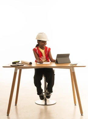 Children experimenting with future professions from a young age, embodying the experience of working as an architect, a portrait of a Saudi Gulf Arab girl wearing a safety vest sitting behind a desk and following the construction plan with focused gestures, white background.