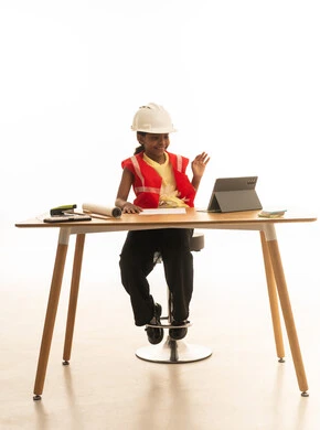 Children experimenting with future professions from a young age, embodying the experience of working as an architect, a portrait of a Saudi Gulf Arab girl wearing a safety vest sitting behind a desk and following the construction plan with focused gestures, white background.