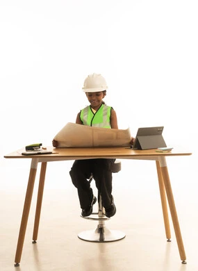 Embodiment of the experience of working as an architect, children experimenting with future professions from a young age, a portrait of a Saudi Gulf Arab girl wearing a safety vest sitting behind a desk and following the construction plan with focused gestures, white background.