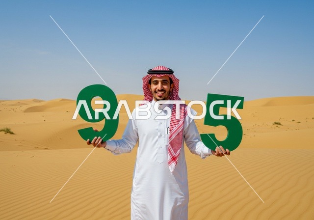 Celebrating national occasions and holidays in nature, Flag Day March 11, Saudi National Day September 23, close-up of a Saudi Arabian Gulf man wearing a traditional shemagh and thobe standing in the desert holding up number sculptures to commemorate the 95th anniversary of Saudi Arabia